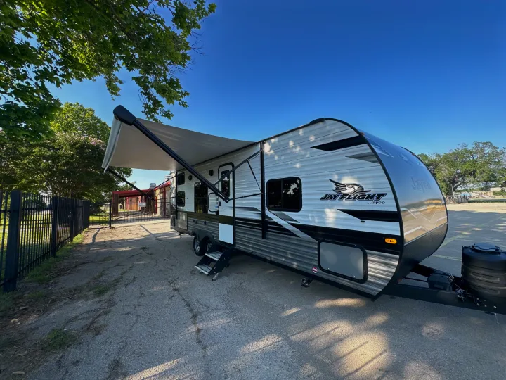A modern white and grey Jayco Jay Flight travel trailer with its awning extended, parked outdoors.. Jayco Jay Flight 2023
