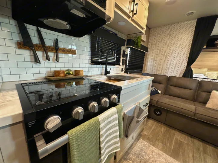 Explore this clean, modern RV rental interior featuring a full kitchen with stove, sink, and a comfortable gray sofa.. Jayco Jay Flight 2023