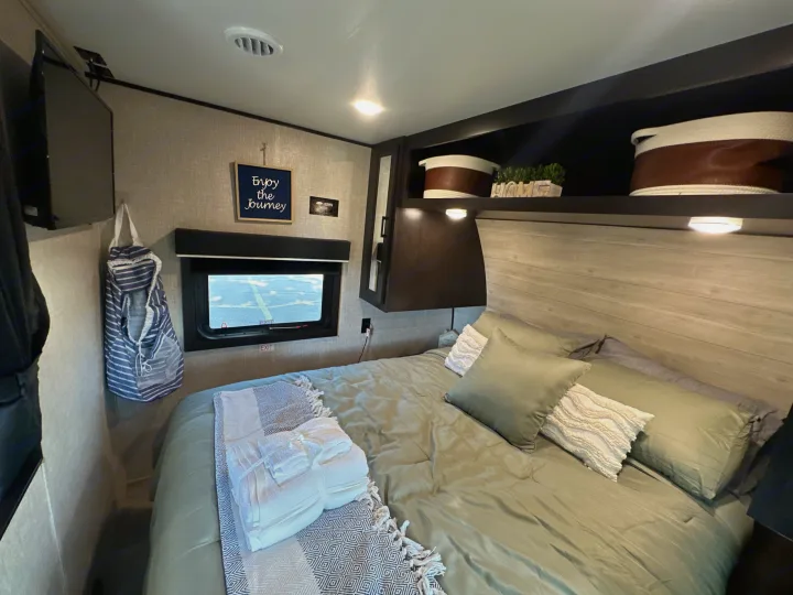 An RV rental's cozy bedroom, complete with a queen bed, TV, window, & homey decor.. Jayco Jay Flight 2023