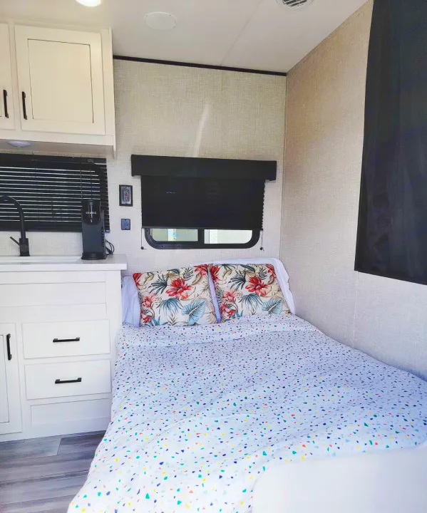 Cozy RV rental interior showing a compact bedroom with floral pillows & a small kitchenette area.. Jayco Jay Flight SLX 2024
