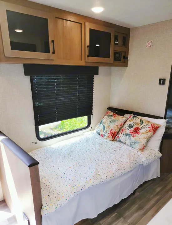RV rental interior featuring a bright bunk bed with colorful bedding, floral pillows, overhead cabinets, and a window.. Jayco Jay Flight SLX 2024