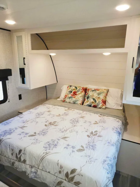 Cozy and compact RV rental bedroom with a floral bedspread, bright lights, and integrated storage.. Jayco Jay Flight SLX 2024