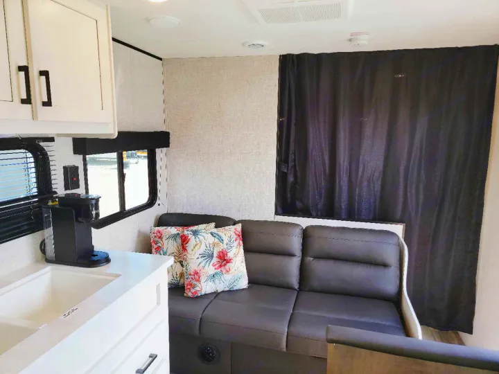 RV rental's living area: white kitchen, sink, coffee maker, comfy dark sofa with tropical pillows & blackout curtains.. Jayco Jay Flight SLX 2024