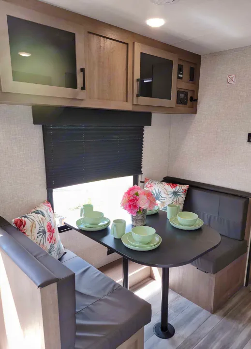 This RV rental features a modern dinette with comfortable booth seating, a table set for dining, and practical overhead storage.. Jayco Jay Flight SLX 2024