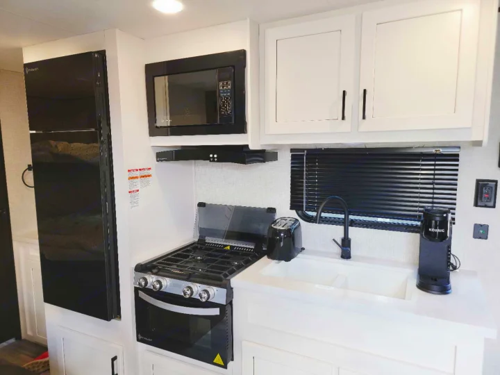 Inside an RV rental: a modern kitchen with white cabinets, sleek black refrigerator, microwave, stove, sink, and coffee maker.. Jayco Jay Flight SLX 2024