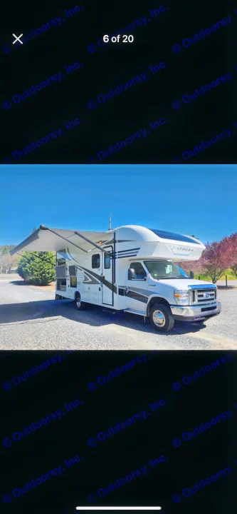 This white Entegra RV rental with its awning extended is parked on a gravel lot under a clear sky, ready for your trip.. Entegra Coach Odyssey 2019