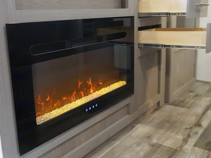 RV rental interior: cozy electric fireplace with amber "flames" and open drawers in light wood cabinetry.. Coleman Lantern 17B 2024