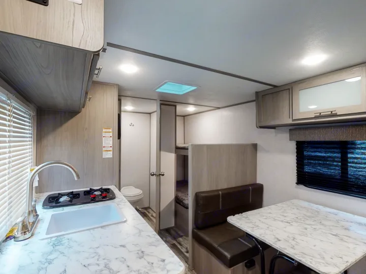Bright rv rental interior with kitchen, dining booth, bunk beds, and a compact bathroom. Ready for your adventures!. Coleman Lantern 17B 2024