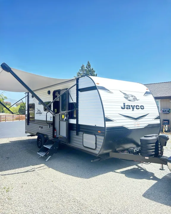 A white and gray Jayco travel trailer for RV rental, parked outdoors with its awning extended under a blue sky.. Jayco Jay Flight 2023