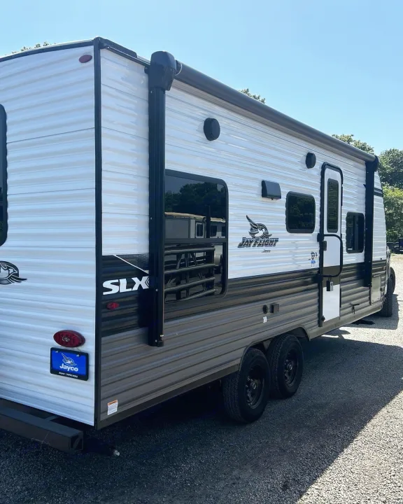 Clean Jay Flight SLX travel trailer, ready for RV rental. Side view shows white and gray exterior, windows, door, and dual axles.. Jayco Jay Flight 2023