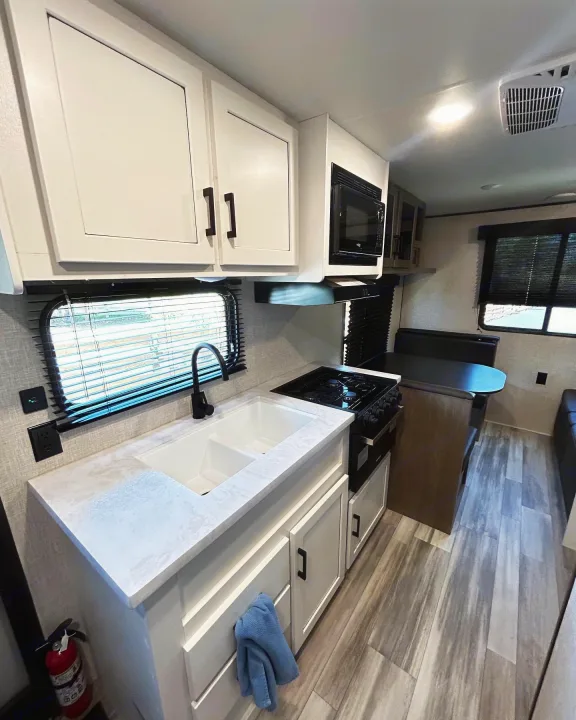 Modern RV rental kitchen with white cabinets, double sink, gas stove, microwave, and dining booth.. Jayco Jay Flight 2023