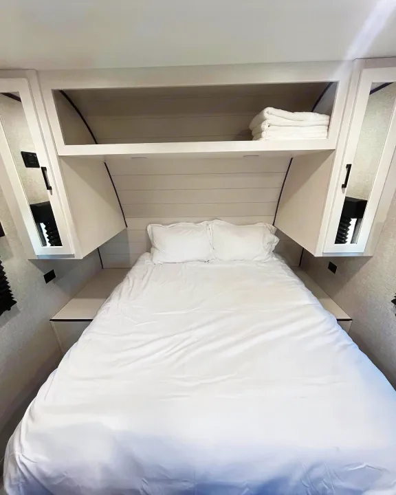 Bright RV rental bedroom with a comfy white bed, overhead shelves for towels, and sleek built-in storage. Ideal compact space.. Jayco Jay Flight 2023