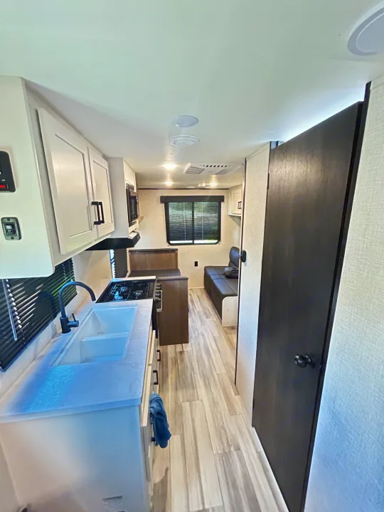 Clean RV rental interior featuring a bright kitchen with double sink & stovetop, ample storage, and comfy dinette seating.. Jayco Jay Flight 2023