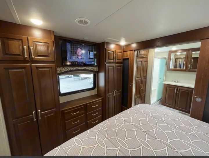 Inside this RV rental: a well-appointed bedroom with ample dark wood storage, TV, and an adjoining modern bathroom.. Keystone RV Alpine 2018