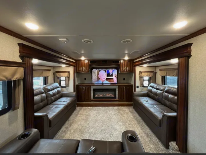 Spacious luxury RV rental living room with two brown leather sofas, central TV/fireplace, and warm wood accents.. Keystone RV Alpine 2018