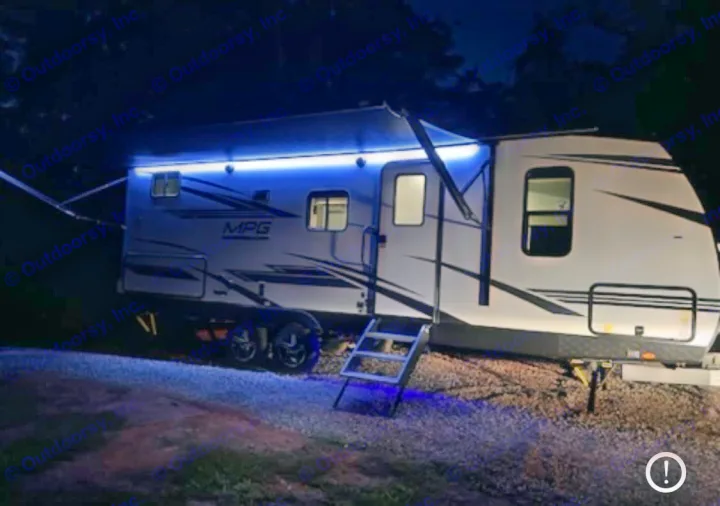 Bright blue awning lights illuminate this RV rental travel trailer and its steps on a dark, gravel campsite.. Cruiser RV MPG 2023
