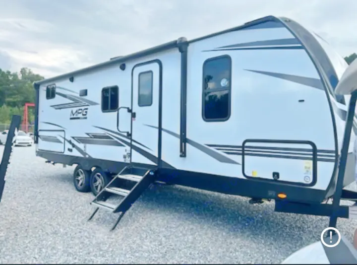 This white MPG travel trailer, ideal for an RV rental adventure, is parked on gravel with its entry steps extended.. Cruiser RV MPG 2023