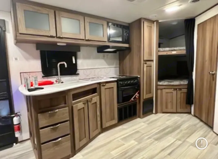 Modern RV rental interior featuring a functional kitchen with a sink, stove, microwave, and cozy bunk beds.. Cruiser RV MPG 2023
