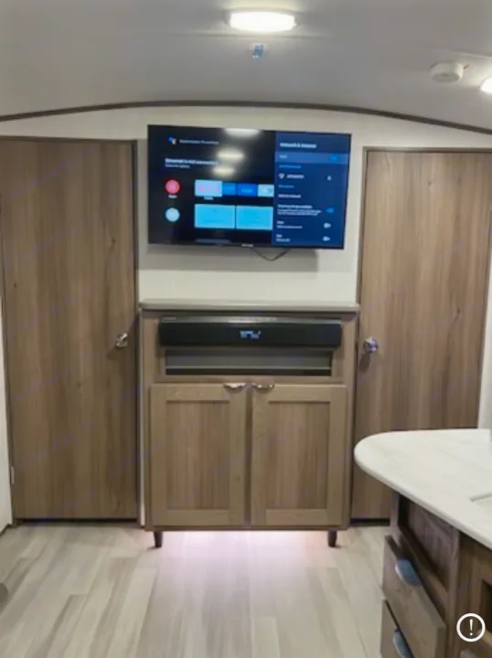 RV rental interior: an entertainment center with a TV, soundbar, and wood cabinets, flanked by two doors.. Cruiser RV MPG 2023
