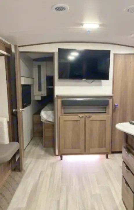Modern rv rental interior with TV, storage cabinets, light flooring, and a compact sleeping bunk visible.. Cruiser RV MPG 2023