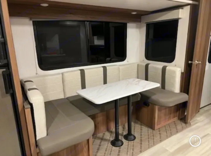 Inside an RV rental, a cozy U-shaped dinette booth with a white table and two-tone seating for dining and relaxation.. Cruiser RV MPG 2023