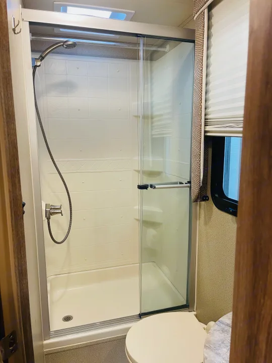 Inside an RV rental, this compact bathroom features a practical shower stall with sliding glass doors and a toilet.. Entegra Coach Odyssey 2019