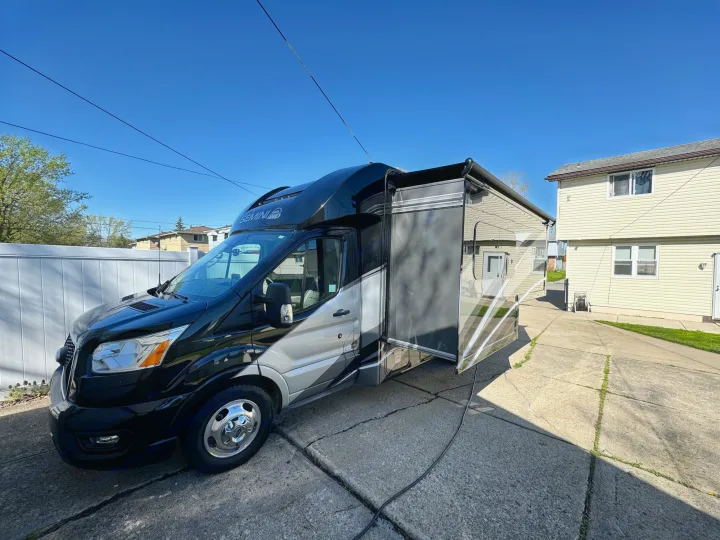 Black and silver Class C RV rental parked on a sunny concrete driveway with its awning extended, ready for adventure.. Thor Gemini 2022