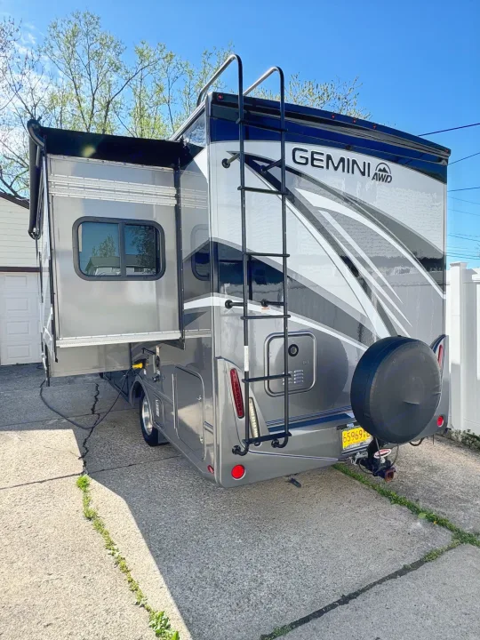 Gray Gemini AWD RV rental parked with its side slide-out extended on a driveway, ready for travel comfort.. Thor Gemini 2022