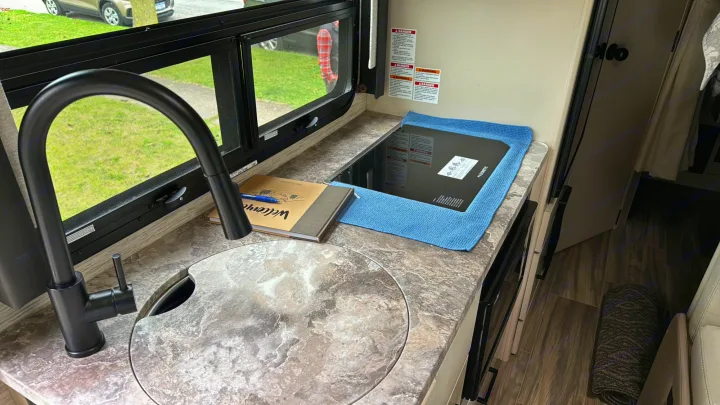 RV rental kitchen area featuring a modern black faucet, covered sink, Dometic cooktop, and a window view.. Thor Gemini 2022