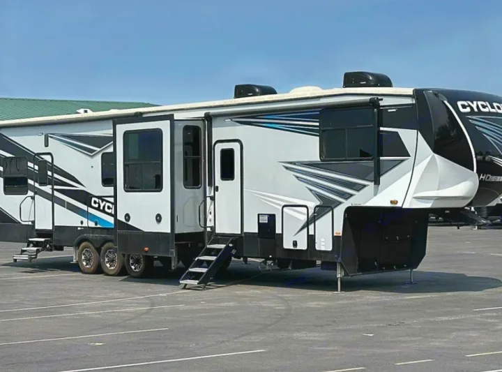 A large, white and black Cyclone fifth-wheel toy hauler RV is set up on asphalt. Ideal for rv rental adventures & camping.. Heartland Cyclone 2022