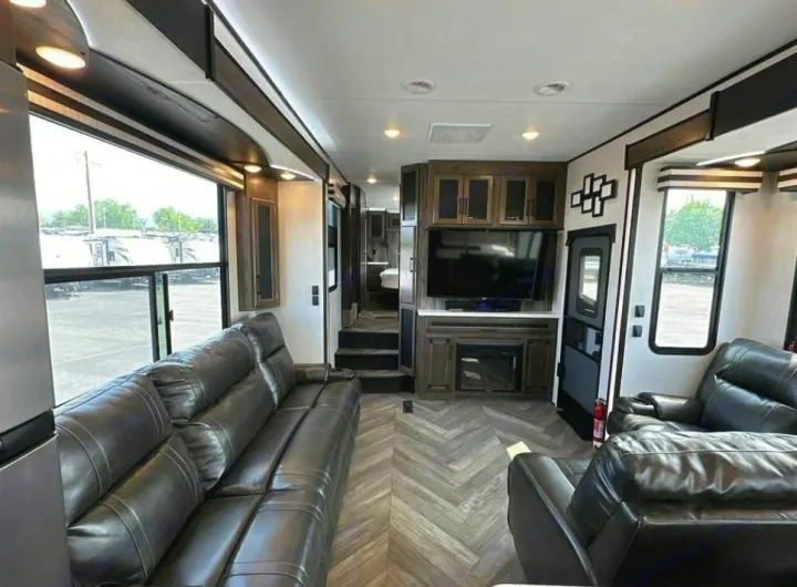 Spacious RV rental interior: features comfortable black leather seating, large windows, and a modern entertainment center.. Heartland Cyclone 2022