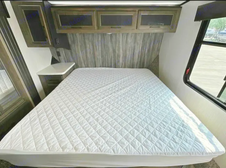 Bright RV rental bedroom featuring a white quilted bed, dark wood cabinets, and an outside view from the window.. Heartland Cyclone 2022