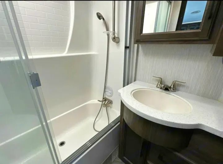 This RV rental bathroom offers a shower-tub combo with glass doors, a vanity with sink, and a mirrored cabinet, maximizing space.. Heartland Cyclone 2022