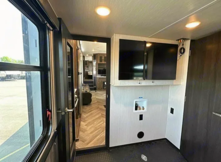 Inside an RV rental: Toy hauler area with washer/dryer hookups, two TVs, and an open doorway to the main living space.. Heartland Cyclone 2022