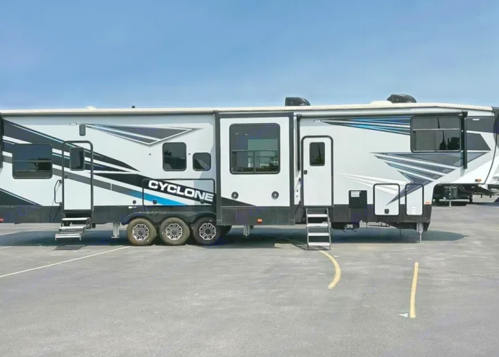 Modern Cyclone toy hauler rv rental on asphalt. This large fifth wheel features grey/black design, multiple slide-outs & steps.. Heartland Cyclone 2022