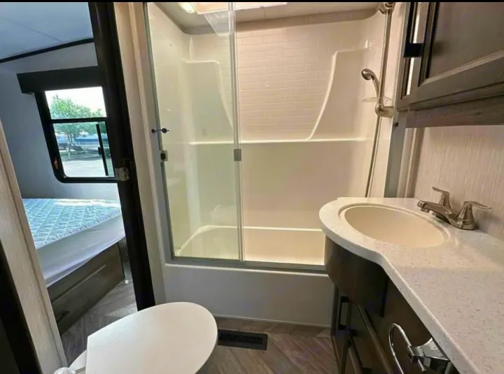 RV rental interior: modern bathroom with glass shower, sink, and toilet, plus a view to the bedroom area.. Heartland Cyclone 2022