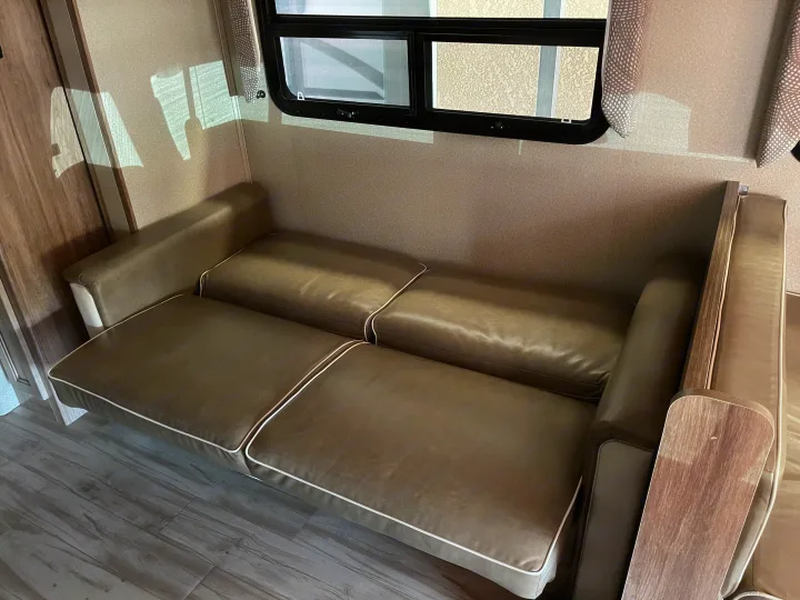 RV rental interior: Spacious brown convertible sofa with white piping, window, and wood-look floor, ideal for your next trip.. Entegra Coach Odyssey 2019