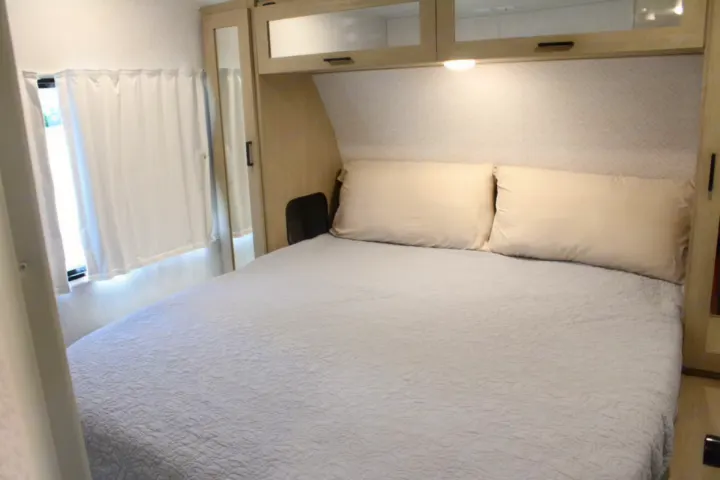 This RV rental bedroom features a comfortable bed with a quilted comforter, overhead storage, and soft lighting, perfect for travel.. Forest River Wildwood Platinum 2024
