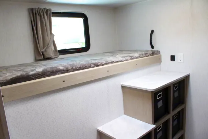Compact RV rental bunk bed area with window, curtain, black handle, and multi-tier storage with cubbies and outlets.. Forest River Wildwood Platinum 2024