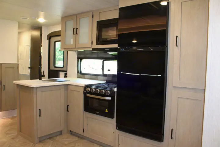 Modern RV rental kitchen with light cabinetry, black appliances, and ample counter space.. Forest River Wildwood Platinum 2024