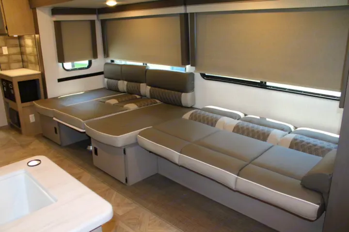 Modern RV rental interior features a convertible dinette/bed, small kitchen counter, and sleek window blinds.. Forest River Wildwood Platinum 2024