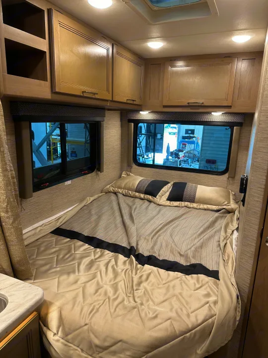 Cozy RV bedroom with a comfortable bed, overhead cabinets, and windows for your next rv rental adventure.. Thor Coleman 2021