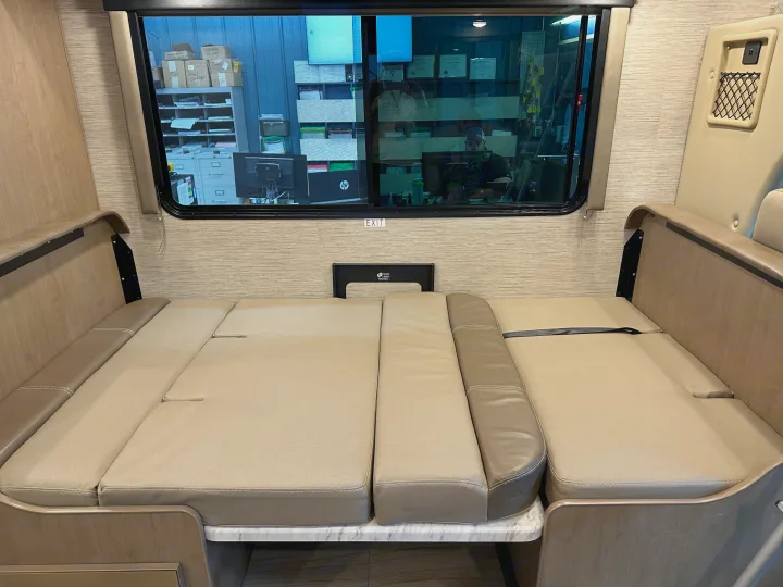 Experience comfort in this RV rental. The versatile dinette seating converts to a bed, visible with light upholstery and wood trim.. Thor Coleman 2021