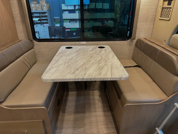 RV rental interior features a comfortable dinette with tan benches, seatbelts, and a marble-look table with cup holders.. Thor Coleman 2021