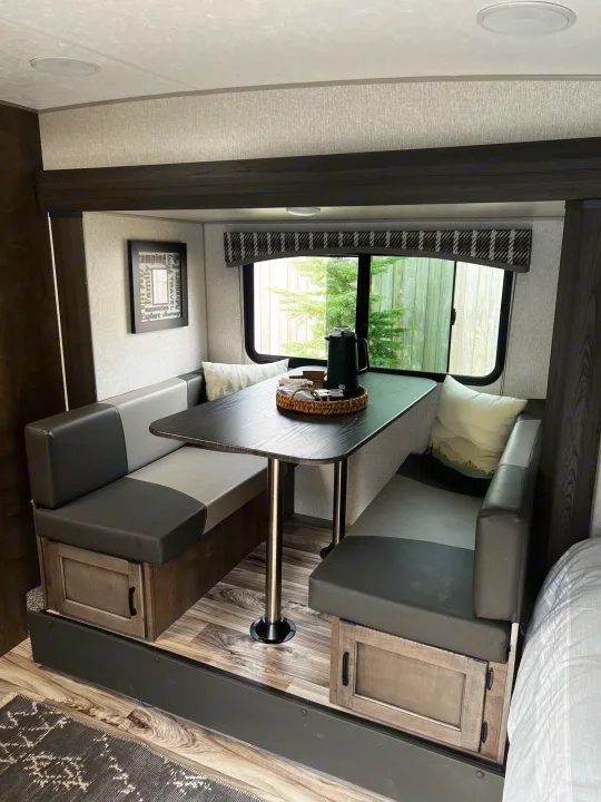 Spacious RV rental dinette with dark table, gray benches, and storage, perfect for meals and relaxation on the road.. Sonic Lite 2022