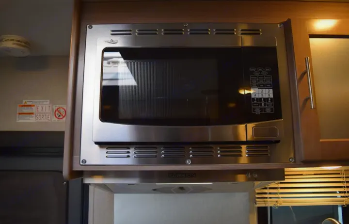 An RV rental's compact kitchen features a modern stainless steel microwave and Furrion range hood, with safety signs nearby.. Adventurer Adventurer 2020