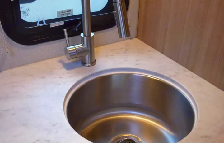 RV rental kitchen: stainless steel sink, modern brushed faucet, light marble-look countertop next to an insulated window.. Adventurer Adventurer 2020