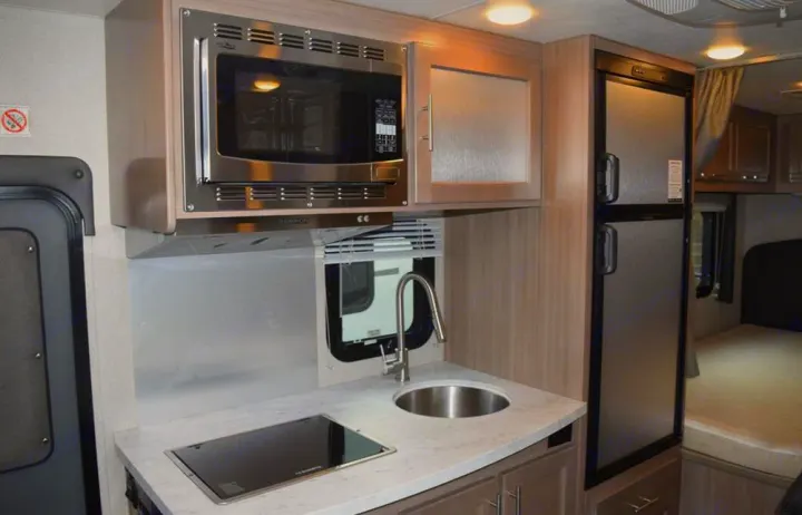 Compact RV rental kitchen features microwave, sink, stovetop, and full-size fridge with adjacent bedroom access.. Adventurer Adventurer 2020
