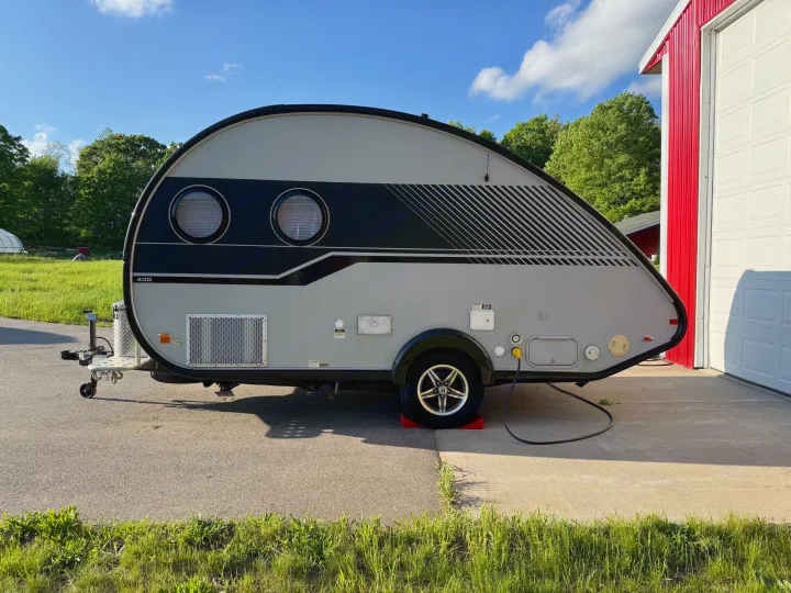 Stylish gray & black teardrop RV rental, a compact travel trailer, parked by a red building, ready for camping.. nuCamp T@B 2018