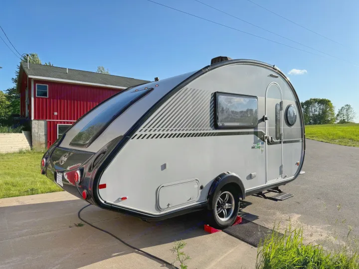 This nuCamp Tab teardrop RV rental is parked on a concrete driveway with a red barn & green field behind. Perfect for adventure!. nuCamp T@B 2018